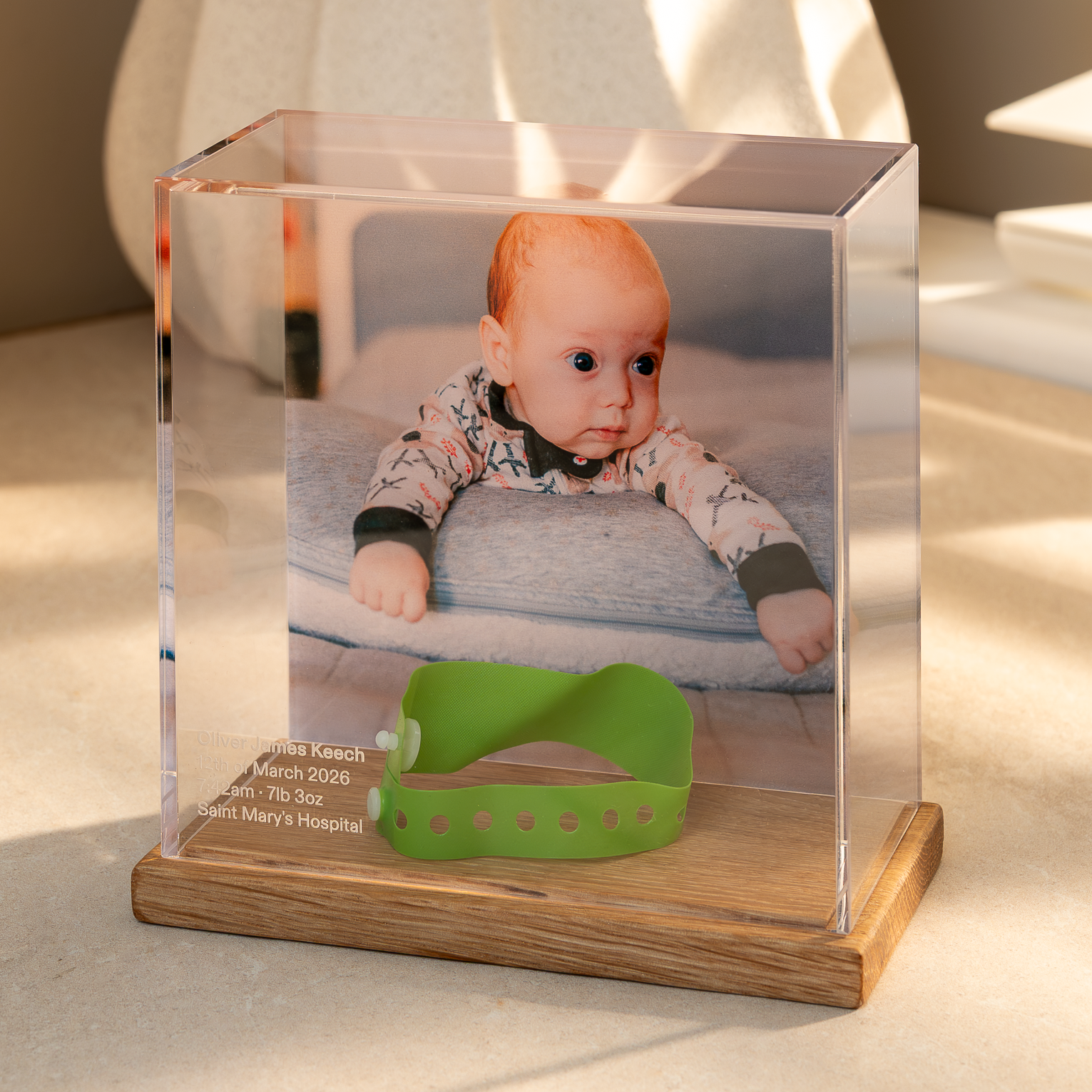 Baby Memory Case with a an Oak base displaying a photo of a baby and a hospital wristband on a light surface.