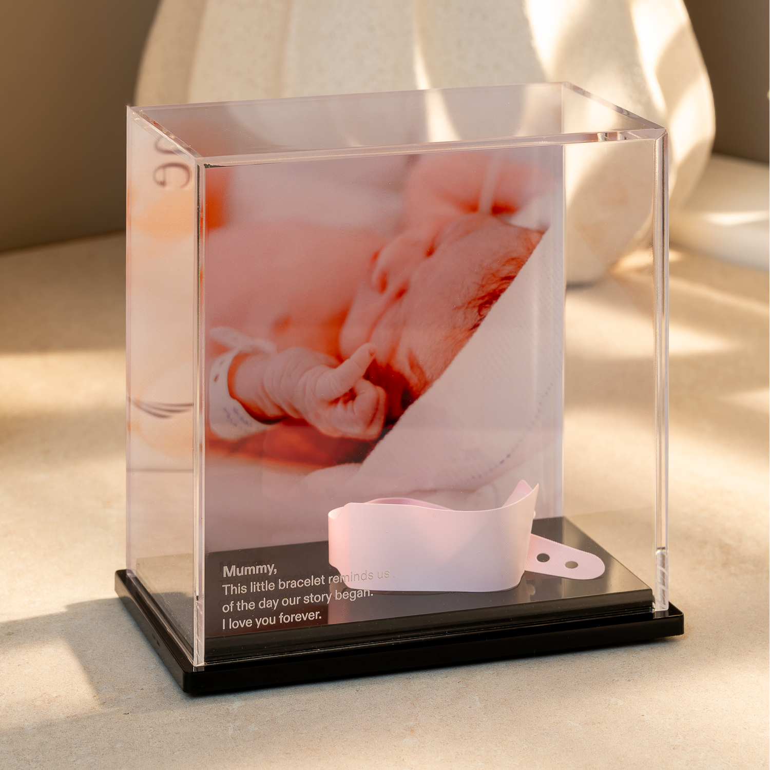 Baby memory display case with a photo of a baby and a hospital wristband inside, on a light surface.