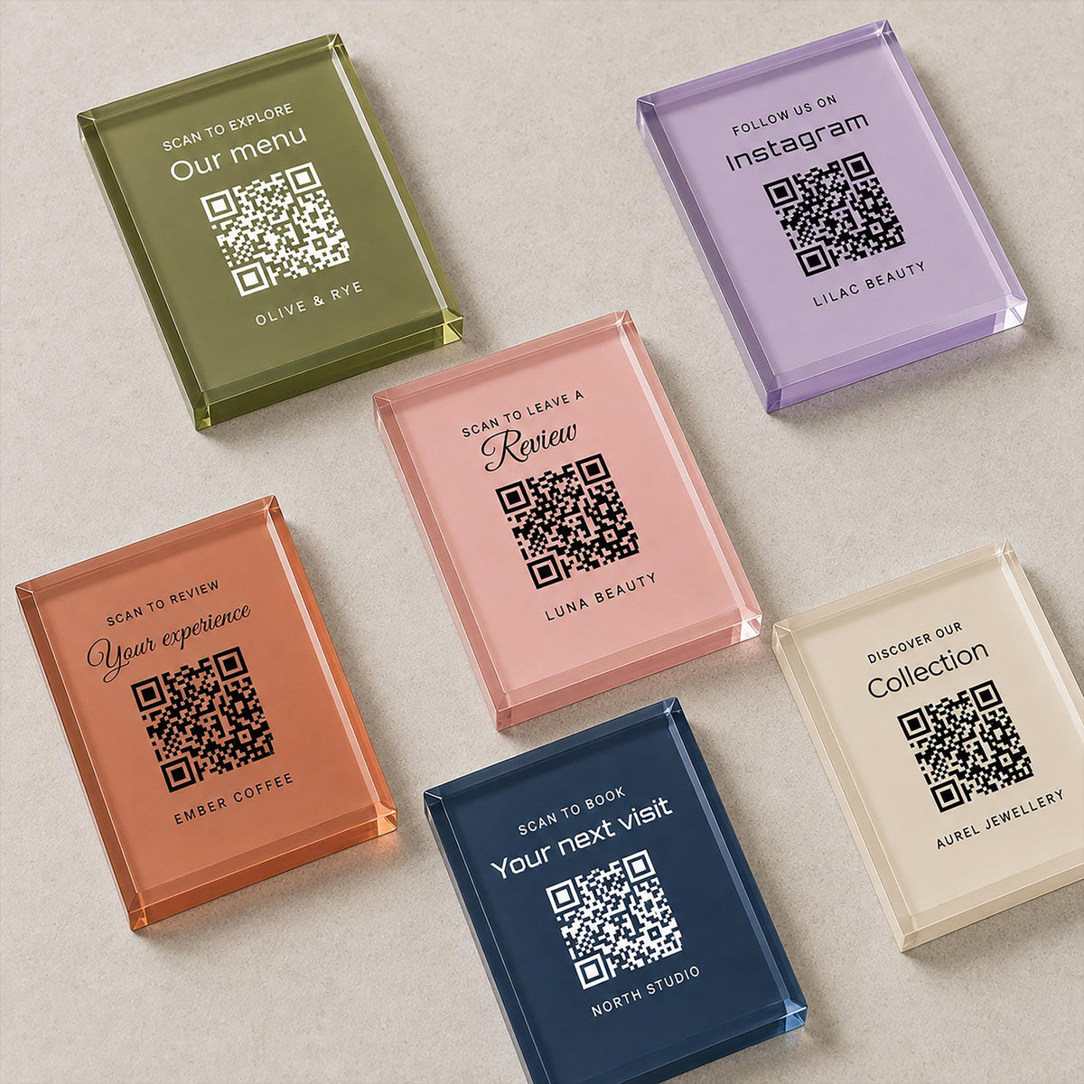 Six coloured acrylic QR code signs laid flat, in olive, lilac, pink, terracotta, navy and ivory, each printed with a different business message.